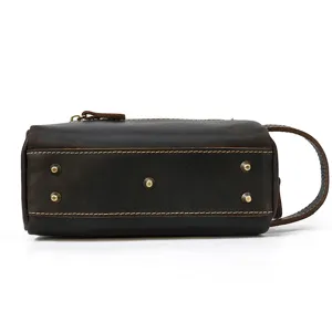 Detail view of brown genuine leather toiletry bag, showing bottom metal feet and side handle.