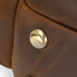 Leather backpack detail close-up, vintage crazy horse cowhide texture with brass rivet hardware.