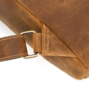 Detailed close-up of genuine crazy horse leather backpack strap, vintage brass hardware.