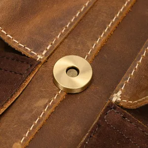 Close-up detail of vintage crazy horse leather backpack with brass magnetic snap and stitching.