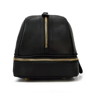 Close-up detail of black leather double zipper toiletry bag showing gold hardware and smooth texture.