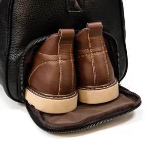 Leather travel bag bottom shoe compartment detail showing brown boots inside zipper pocket.