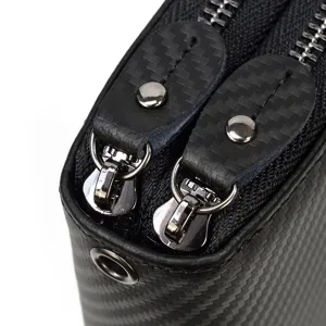 Detalle de cerca de cartera larga para hombre con patron de fibra de carbono y cremalleras.