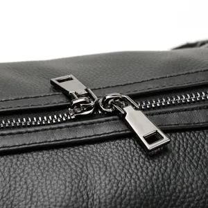 Detailopname van de duurzame metalen ritssluiting en zwarte leertextuur op de reistas voor heren.
