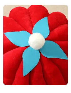 Primer plano detallado de cama para gatos con diseño de calabaza roja, hojas azules y pompón blanco.