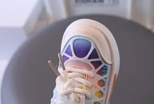 Macro detail view of the rainbow gradient mesh and white laces on children's sneakers.