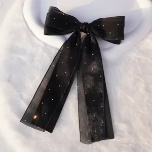 Elegante horquilla de lazo doble negro con diamantes de imitación sobre fondo de felpa