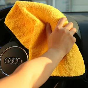 Detailed view of soft yellow microfiber car cleaning towel wiping interior steering wheel.