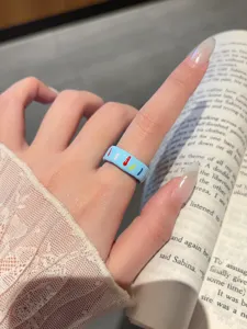 Close up view of light blue enamel ring with colorful details worn on hand model reading book