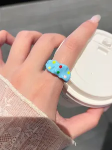 Detailed close-up of a sweet blue oil-dropping ring with colorful polka dots on a finger.
