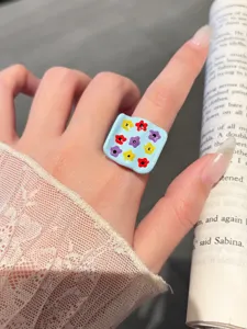Detailed close-up shot of a sweet blue oil-drop ring with colorful flower patterns worn on finger.