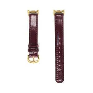 Gros plan sur les détails du bracelet de montre en cuir bordeaux brillant doré.