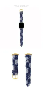 Dettaglio cinturino orologio in denim scozzese con texture di stoffa e fibbia dorata.