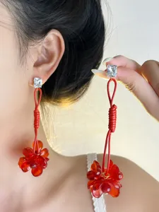Primo piano dettagliato di lunghi orecchini con nappe floreali rosse e brillanti perle di cristallo.