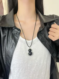 Close-up detail shot of a fashionable black gourd pendant necklace worn gracefully on neck.
