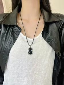 Close-up detail shot of a black gourd pendant necklace worn on neck with leather jacket.