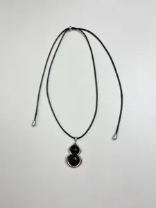 Black gourd pendant necklace detail view, smooth metal frame with black beads, adjustable cord.