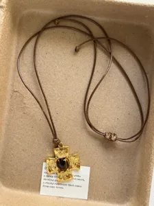 Closeup of vintage gold cross pendant necklace with heart gemstone and brown cord detail.