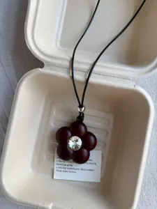 Close-up of a dark red flower pendant necklace with crystal center in a pulp box.