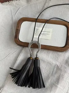 Black leather tassel necklace detail shot, long pendant style with metallic accent element.