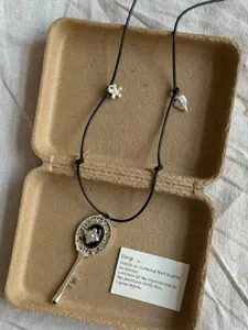 Vintage key pendant necklace with black cord and cute floral charms for detailed look.