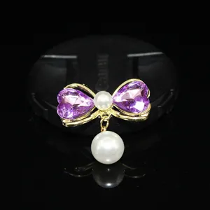 Close up of a gold tone bow accessory featuring purple heart crystals and dangling pearls.