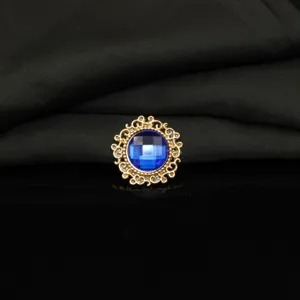 Close-up detail of a vintage gold alloy rhinestone button with a central blue faceted gem.