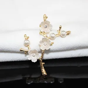 Gold alloy branch brooch with white plum flower petals, faux pearls and sparkling rhinestones.