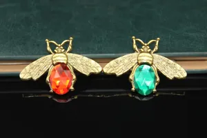 Close up of DIY rhinestone bee accessories with red and green gems for phone case decoration.