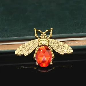 Detail shot of a vintage gold-toned bee alloy charm with a vibrant red crystal stone for DIY crafts.