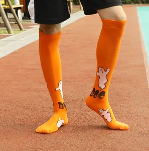 Close-up detail shot of orange Halloween ghost pattern knee high socks worn on leg outdoors.