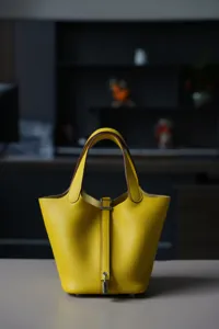 Gele lederen emmertas met handvat en metalen sluiting, klassieke damestas voor dagelijks.