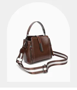 Nahaufnahme der braunen Echtleder Handtasche mit gestreiftem Schultergurt und edlem Metallverschluss.