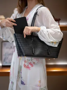 Grand sac cabas noir perforé avec pochette intérieure assortie et poignées fines élégantes.