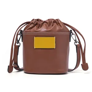 Genuine leather brown bucket bag with drawstring closure, stylish shoulder strap and front patch.