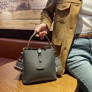 Grey leather bucket bag detail, wide strap and chic front buckle, premium handbag style.