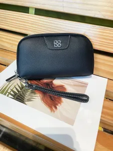 Close up of black genuine leather wristlet wallet featuring chic metal flower accent and zipper.