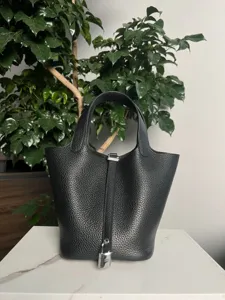 Vue détaillée du sac seau en cuir noir avec serrure argentée sur fond de marbre blanc.