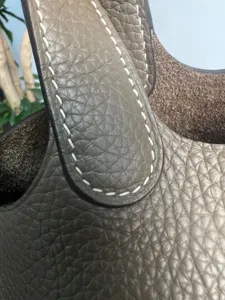 Dettaglio borsa secchiello in vera pelle con grana naturale e cuciture cerate bianche.