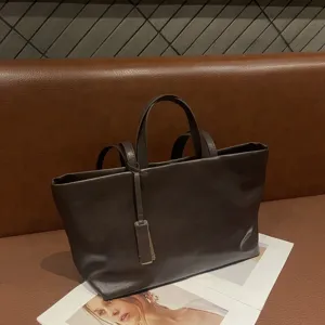 Brown leather tote bag detail showing soft texture, double top handles and chic minimalist design.