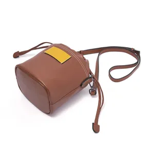 Brown leather bucket bag detail showing contrast stitching, drawstring closure, and shoulder strap.
