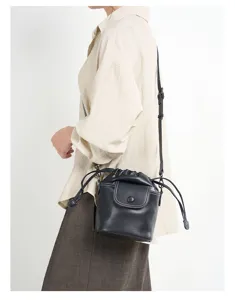 Black genuine leather bucket bag with drawstring closure and stylish flap for women.