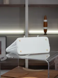 Détail du fond de sac cabas en cuir perforé blanc avec pieds en métal et finition ajourée.