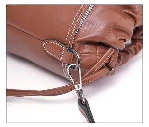 Brown leather bucket bag detail view showcasing metal clasp, strap, and contrast stitching.