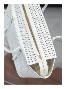 Gros plan détaillé du sac à main en cuir perforé blanc avec fermeture éclair dorée.