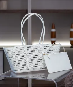 Gros plan d'un sac cabas en cuir blanc perforé avec pochette assortie sur verre.