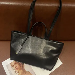 Black leather tote bag detail showing soft texture, dual handles and large capacity design.
