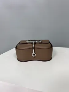 Brown textured leather mini crossbody bag detail showing unique metal lock and curve design.