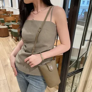 Detailed close-up view of genuine leather crossbody phone bag worn by model in a cozy cafe.