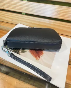 Detailed view of the black genuine leather wristlet clutch showing fine texture and white stitching.